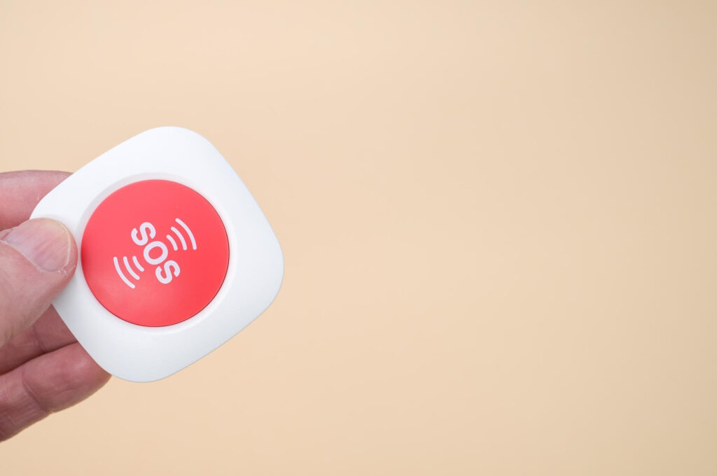 Hand holding red SOS emergency button on beige background